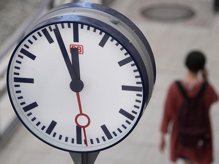 Eine Frau geht hinter einer Bahnhofsuhr auf einem Bahnsteig entlang. Foto: Sebastian Kahnert/Archivbild