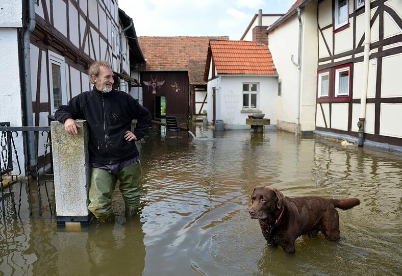 Ein Hund steht mit seinem Herrchen auf einem überfluteten Grundstück in Altenburschla (Hessen).