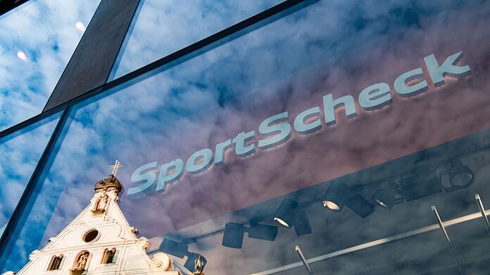 In der Fassade einer SportScheck-Filiale in der Münchener Fußgängerzone spiegelt sich ein Haus.