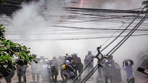 Demonstranten tragen in Rangun in einer Wolke von Tränengas Schutzhelme, um sich gegen die Gewalt zu schützen.
