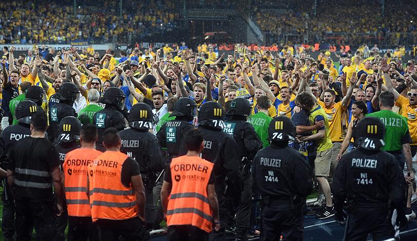 Braunschweiger Fans stehen Polizisten und Ordnern nach dem Abpfiff auf dem Platz gegenüber.