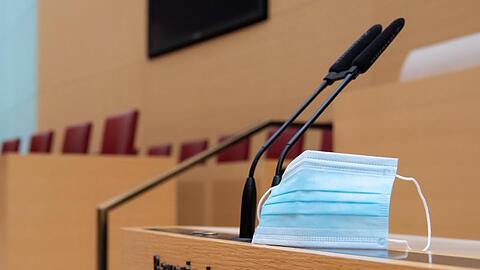 Ein Mund-Nase-Schutz befindet sich im Plenarsaal im bayerischen Landtag neben Mikrofonen. Foto: Sven Hoppe/dpa/Illustration