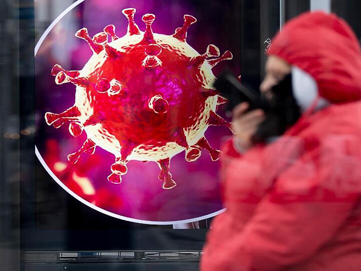 Eine elektronische Werbetafel zeigt eine Illustration des Coronavirus. Foto: Christoph Soeder/dpa/Symbolbild
