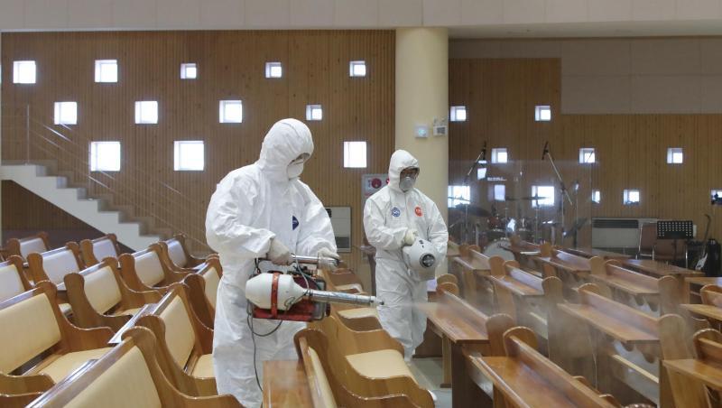 Zwei Arbeiter in Schutzkleidung versprühen Desinfektionsmittel in einer Kirche in Südkorea. Zwei Arbeiter in Schutzkleidung versprühen Desinfektionsmittel in einer Kirche in Südkorea.