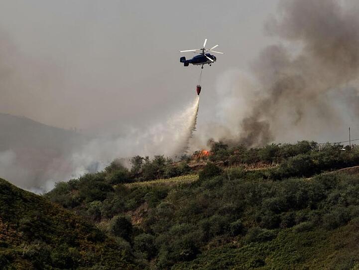 Ein Löschhubschrauber im Einsatz über einem bewaldeten Hang.