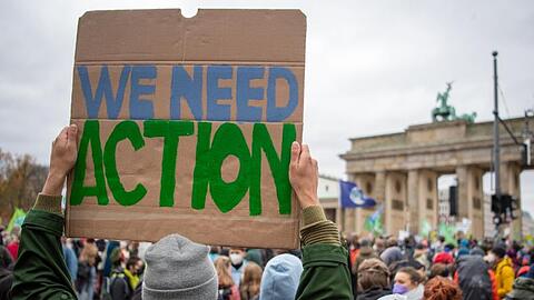 "We need Action": Ein Teilnehmer mit einem Transparent vor dem Brandenburger Tor.
