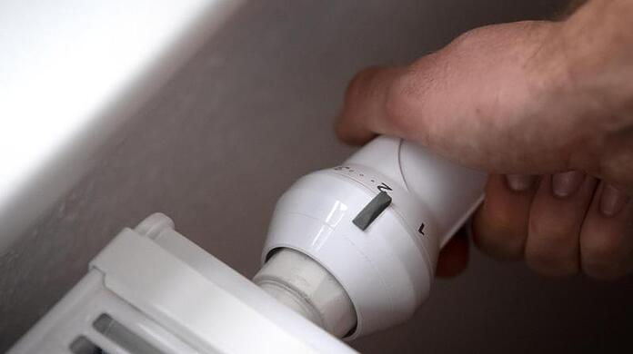 ILLUSTRATION - Ein Mann dreht am Thermostat einer Heizung. Die Großhandelspreise für Erdgas steigt und steigt.