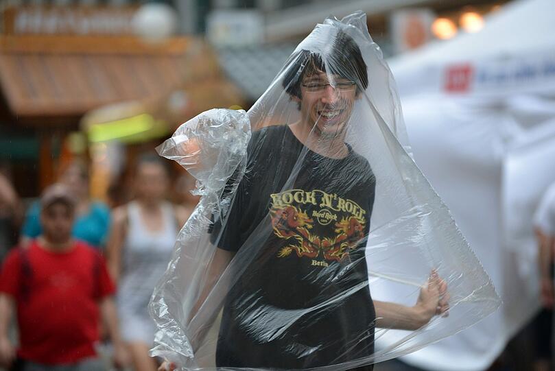 Hessentagsbesucher mühen sich am 20.06.2013 in Kassel (Hessen) im Gewitterregen ab, einen Plastik-Regenschutz anzulegen. Ein Gewitter zog am Nachmittag über die Stadt und vertrieb die größte Hitze.