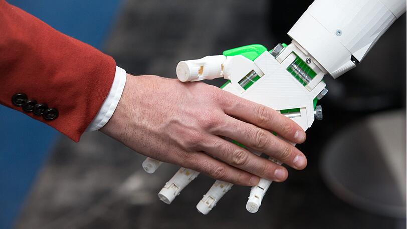 Ein humanoider Roboter gibt einem Menschen die Hand am Stand von ioX Lab bei der IT-Messe CeBIT. (Symbolbild)
