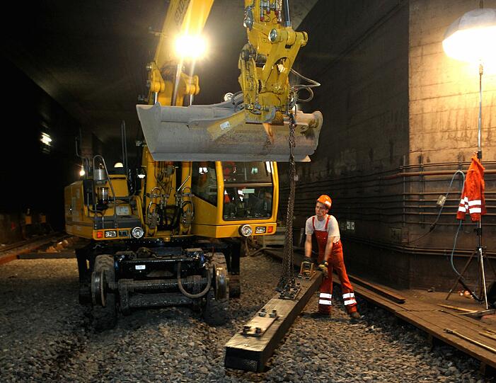 Schwerstarbeit: Ein Arbeiter hebt ein Bauteil für den Bagger an.