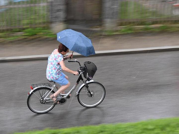 Mit einem Regenschirm trotzt eine Radfahrerin im bayerischen Garmisch-Partenkirchen dem Regen.