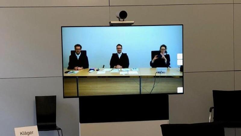 Mitglieder der 7. Zivilkammer am Landgericht München sind im Sitzungssaal 155 auf einem Monitor zu sehen.
