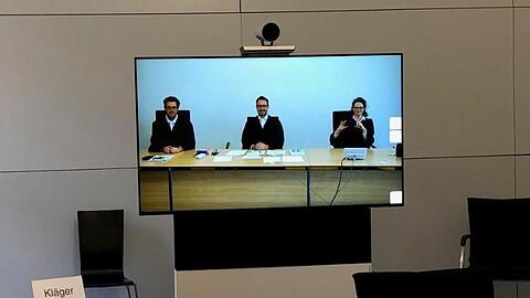 Mitglieder der 7. Zivilkammer am Landgericht München sind im Sitzungssaal 155 auf einem Monitor zu sehen.