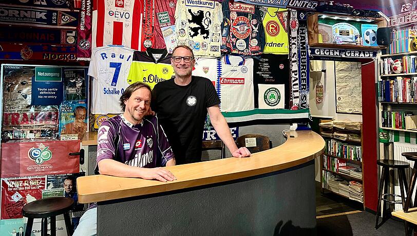 Seit 20 Jahren gibt es das Stadion an der Schleißheimer Straße. An den Wänden hängen viele Trikots und Schals – von Fans gespendet. Im "Stadion" seien Anhänger aller Vereine willkommen, sagen die Betreiber Holger "Holle" Britzius (l.) und Michael "Michel" Jachan.