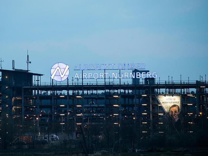 Der Schriftzug "Albrecht-Dürer-Airport" leuchtet auf dem Parkhaus des Flughafens Nürnberg. Foto: Daniel Karmann/Archiv