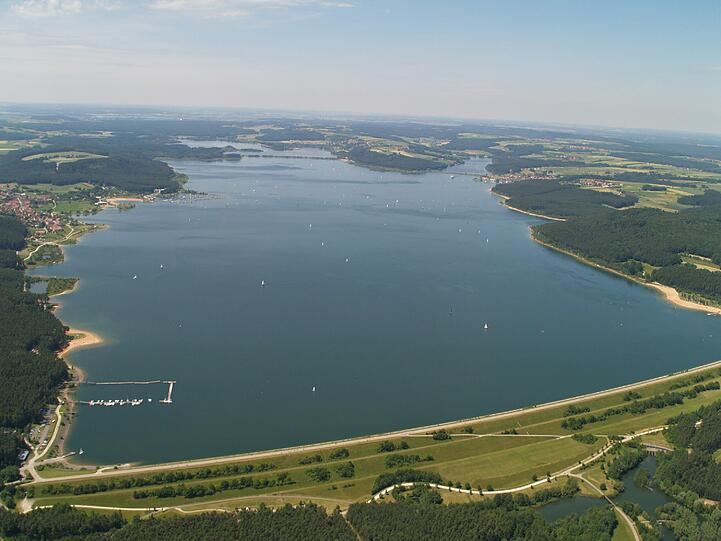 So präsentiert sich der Große Brombachsee heute seinen Besuchern: Am linken Ufer ist der Ort Ramsberg mit seinem kleinen Segelhafen (unten) zu sehen. Am gegenüberliegenden Ufer der von Wald gesäumte Sandstrand.