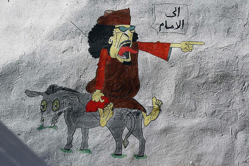 Hier sitzt Gaddafi rücklinks auf einem Esel, dem er vergeblich den Befehl "Jetzt lauf schon!" zubrüllt. Die Rebellen nutzen die neuen Freiheiten seit Beginn der Ausschreitungen und machen sich in der Öffentlichkeit künstlerisch über Gaddafi lustig.