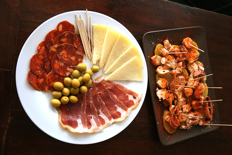 Tapas gibt&rsquo;s nach wie vor in der &bdquo;Bar Triana&ldquo;: Links Chorizo, Serrano,
Rioja-Käse und Oliven, nebendran ein Teller &bdquo;Pulpo a la gallega&ldquo;.