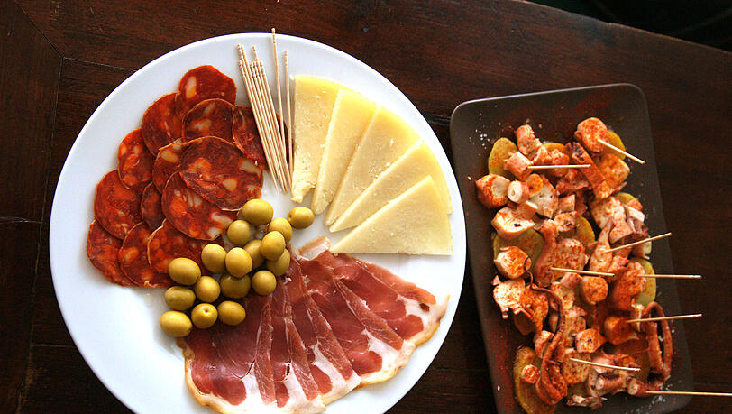 Tapas gibt&rsquo;s nach wie vor in der &bdquo;Bar Triana&ldquo;: Links Chorizo, Serrano,
Rioja-Käse und Oliven, nebendran ein Teller &bdquo;Pulpo a la gallega&ldquo;.