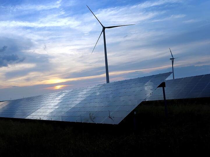 Abendhimmel spiegelt sich auf den Solarzellen einer vor Windrädern stehenden Solarkraftanlage. Foto: Karl-Josef Hildenbrand/Archivbild
