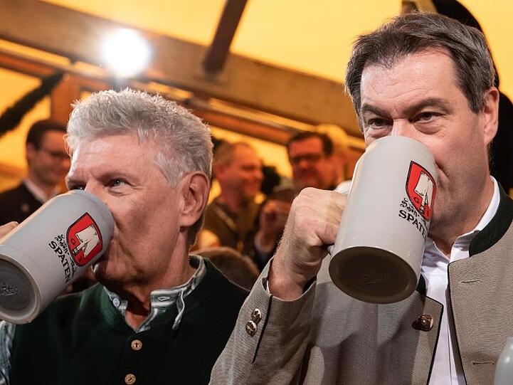 Markus Söder (r, CSU) und Dieter Reiter (SPD) trinken zusammen Bier aus Maaskrügen.