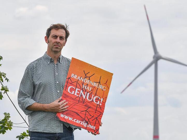 Eigenheimbesitzer Stefan Hellert auf seinem Grundstück. In rund 1500 Metern Entfernung dreht sich der Rotor einer Windenergieanlage.