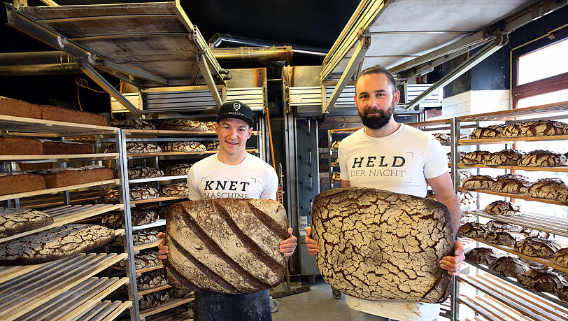 Nico Scheller und Manuel Grundei stemmen ihre großen neun Kilo schweren Brotlaibe. Den verführerischen Duft muss man sich dazudenken.