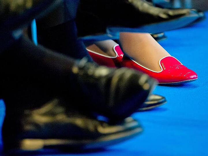 In roten Schuhen sitzt eine Frau zwischen Männern in dunklen Anzügen und passendem Schuhwerk. Foto: Tim Brakemeier/Archiv
