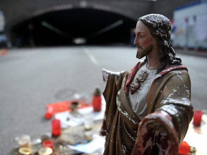 Verwelkte Blumen und eine Jesusstatue weisen den Unglucksort aus.