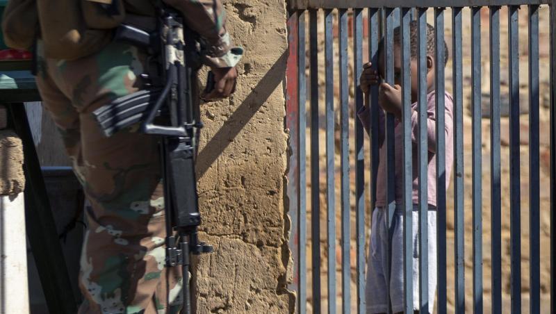 Ein Kind hält sich im südafrikanischen Johannesburg an einem Torgitter fest, hinter dem ein Mitglied der Nationalen Verteidigungskräfte steht. Ein Kind hält sich im südafrikanischen Johannesburg an einem Torgitter fest, hinter dem ein Mitglied der Nationalen Verteidigungskräfte steht.