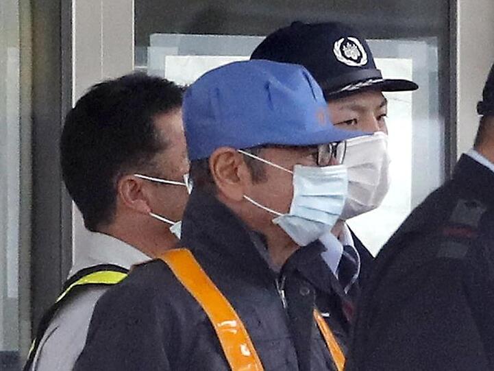 Ein maskierter Mann mit blauer Mütze, von dem man annimmt, dass es sich um den ehemaligen Nissan-Vorsitzenden Ghosn handelt, verlässt mit Sicherheitskräften das Tokyo Detention Center.
