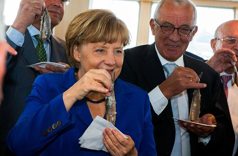 Halbe Sachen sind nichts für die Bundeskanlerin. Sie greift zum Matjes am Stück. "Bin ja mal gespannt, wie sie den jetzt runterschlingt", scheint sich der Herr hinter ihr zu denken.