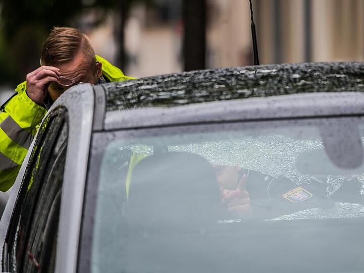 Zwei Polizeibeamte begutachten ein Fahrzeug mit beschädigter Heckscheibe im abgesperrten Bereich. In der Innenstadt von Rüsselsheim kam es zu Schüssen.