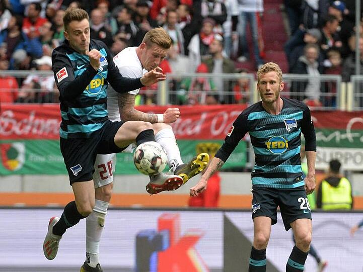 Andre Hahn (M) von Augsburg und Herthas Lukas Klünter (l) kämpfen um den Ball, beobachtet von Fabian Lustenberger. Foto: Stefan Puchner