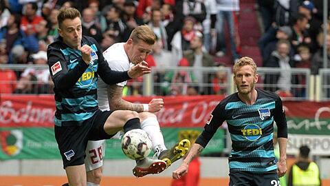Andre Hahn (M) von Augsburg und Herthas Lukas Klünter (l) kämpfen um den Ball, beobachtet von Fabian Lustenberger. Foto: Stefan Puchner