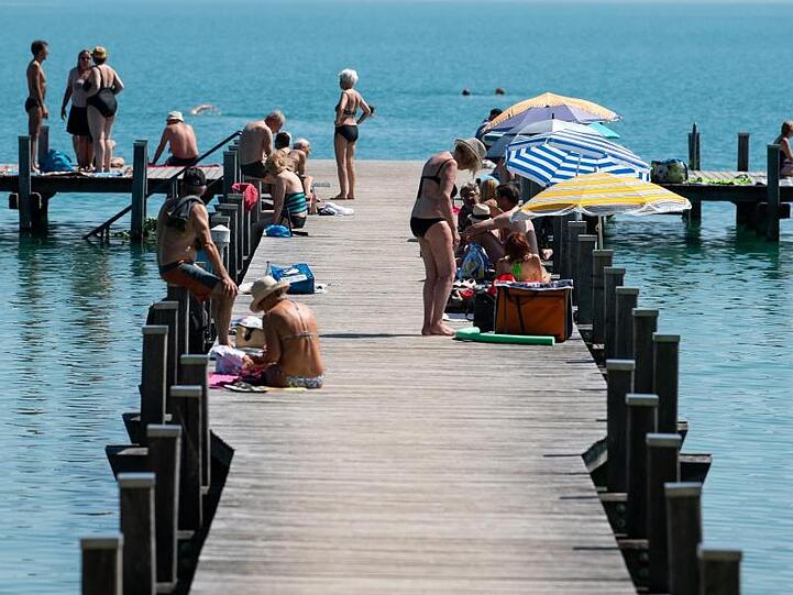 Zahlreiche Ausflügler sitzen bei Sonnenschein und hohen Temperaturen auf einem Steg am Wörthsee.