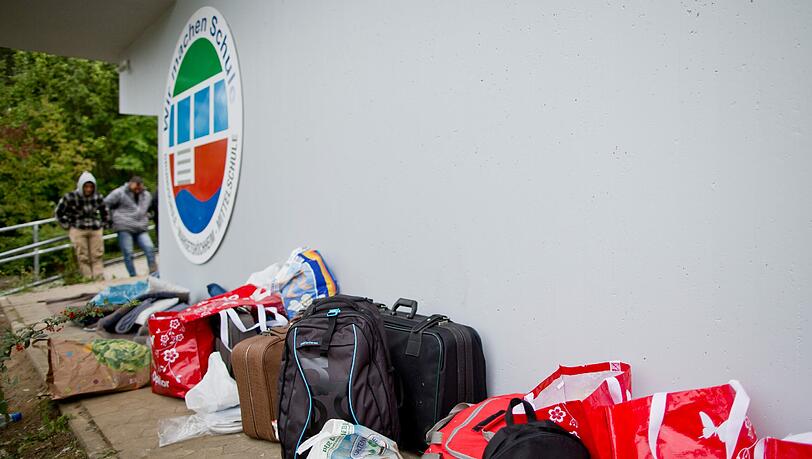 Mehrere Taschen von Flüchtlingen stehen vor einer Schulsporthalle in Margetshöchheim, die als Notunterkunft dient. Fast ein Dutzend Flüchtlinge hatten in der Nacht zu Dienstag vor der Halle mit einem nächtlichen Sitzstreik für eine schnellere Bearbeitung ihrer Asylanträge protestiert. Mehrere Taschen von Flüchtlingen stehen vor einer Schulsporthalle in Margetshöchheim, die als Notunterkunft dient. Fast ein Dutzend Flüchtlinge hatten in der Nacht zu Dienstag vor der Halle mit einem nächtlichen Sitzstreik für eine schnellere Bearbeitung ihrer Asylanträge protestiert.