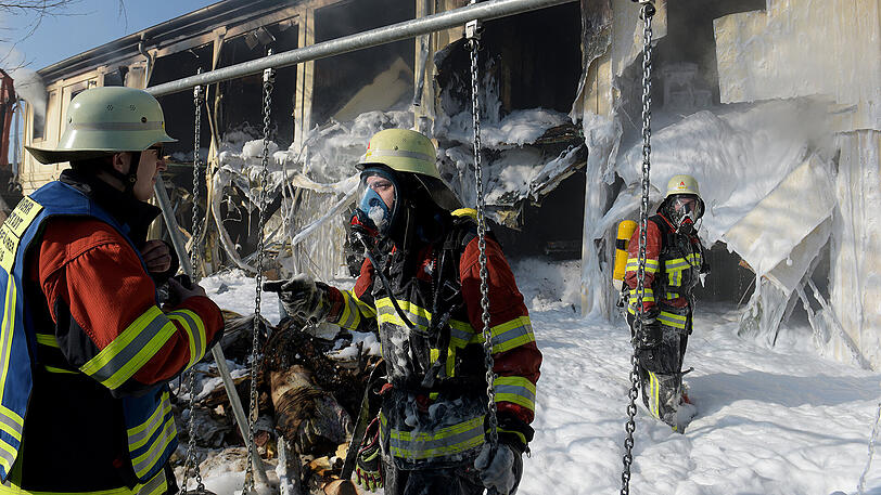Feuerwehrleute stehen vor ausgebrannten Wohncontainern. Nachts kam es in dieser Asylunterkunft aus unbekannter Ursache zu einem Brand, bei dem drei Bewohner verletzt wurden.