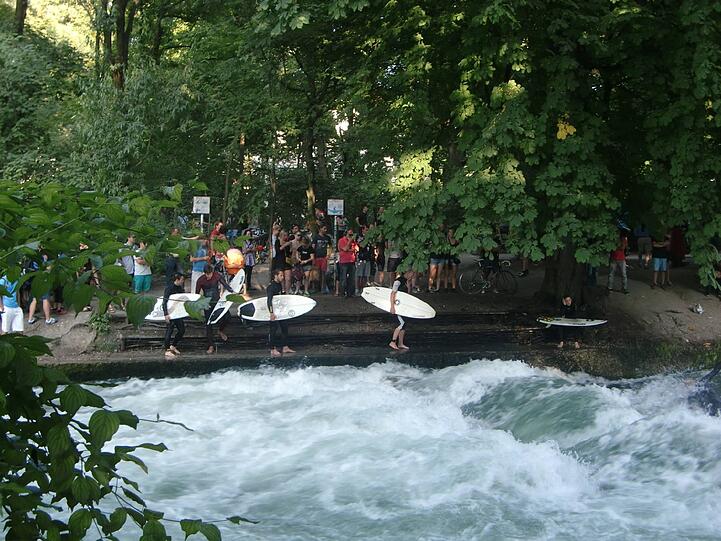 Von links und rechts stehen die Surfer an, um als nächster auf die Welle zu springen. Von der Brücke der Prinzregentenstraße werden sie immer von viele Schaulustigen beobachtet.