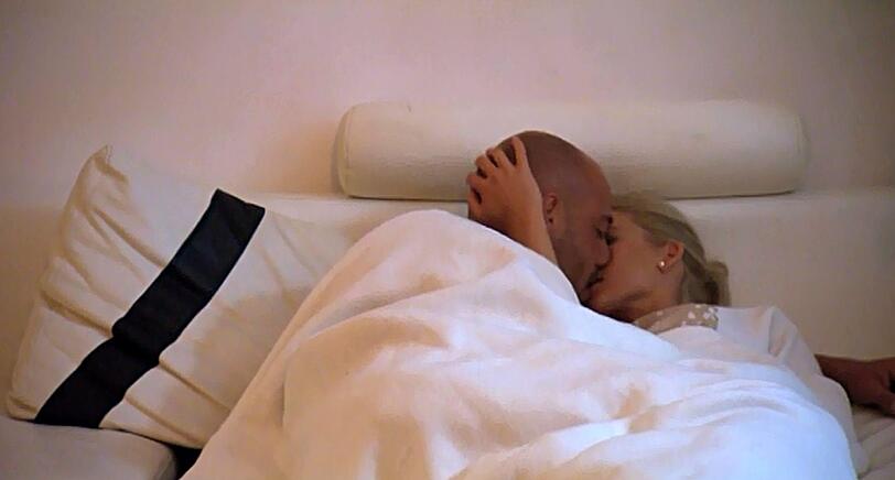 Christian und Katja knutschen und kuscheln unter der Decke.