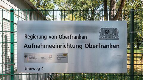 Ein Hinweisschild der Aufnahmeeinrichtung Oberfranken hängt am Zaun der Flüchtlingsunterkunft.