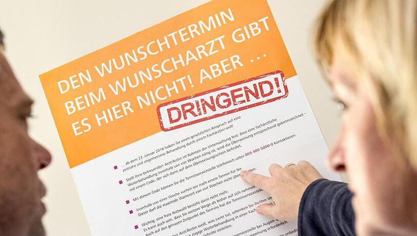 Ein Mann und eine Frau betrachten ein Plakat mit Hinweisen zu der Einführung von "Terminservicestellen". Ein Mann und eine Frau betrachten ein Plakat mit Hinweisen zu der Einführung von "Terminservicestellen".