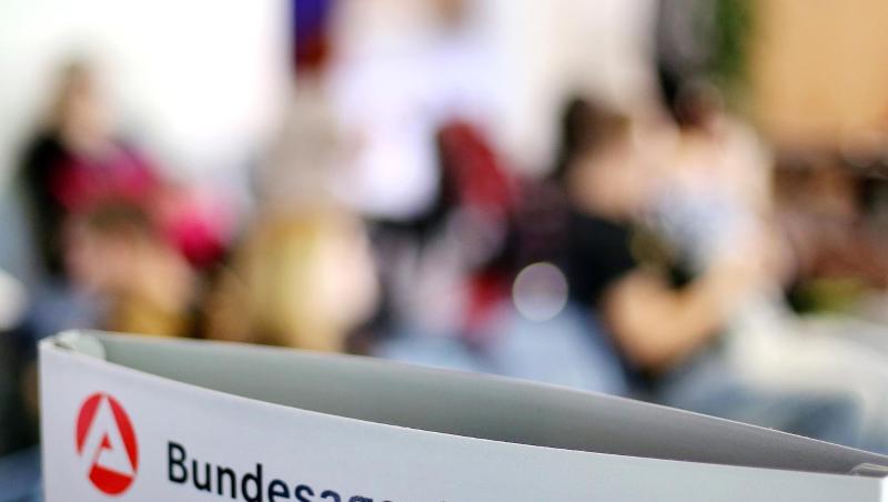 Ein Schild mit der Aufschrift "Bundesagentur für Arbeit" steht einem vollen Wartezimmer im Jobcenter. Ein Schild mit der Aufschrift "Bundesagentur für Arbeit" steht einem vollen Wartezimmer im Jobcenter.