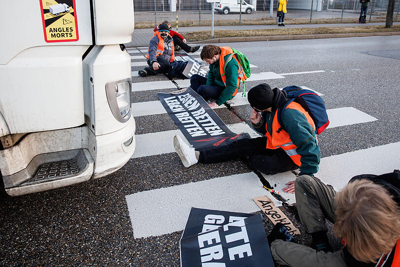 Aktivisten der Gruppe "Die letzte Generation" haben sich mit ihren Händen auf einen Zebrastreifen auf der Südallee, einer Zufahrt zum Frachtbereich vom Münchner Flughafen, geklebt.