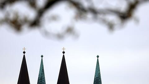 Die Kirchtürme des Würzburger Doms zeichnen sich vor dem bewölktem Himmel ab.