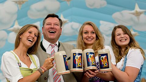 Während draußen noch gehämmert wird, präsentieren Lisa, Anna, und Sarah (l-r) zusammen mit Wiesn-Chef Josef Schmid (CSU) im Hackerzelt den Wiesn-Maßkrug.