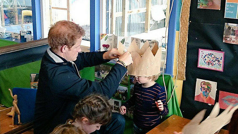 Prinz Harry platziert liebevoll eine Papierkrone auf dem Kopf des Jungen Prinz Harry platziert liebevoll eine Papierkrone auf dem Kopf des Jungen