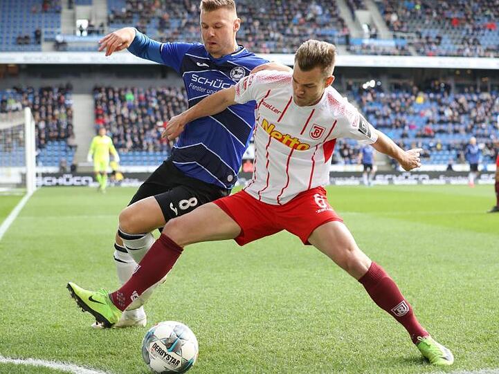 Bielefelds Florian Hartherz (l.) im Kampf um den Ball mit Benedikt Saller (r.) aus Regensburg. Foto: Friso Gentsch/dpa