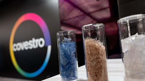 Eine deutsche Firma wird arabisch: Das Logo des Spezialchemie-Konzerns in einem Firmen-Showroom, davor Gläser mit Covestro-Materialien.