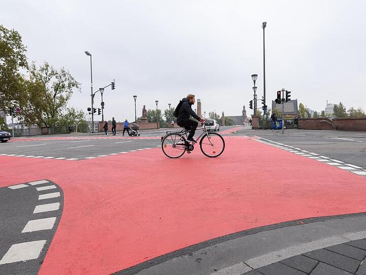 Ein Mann fährt mit einem Fahrrad auf einem rot gekennzeichneten Fahrradweg über eine Straßenkreuzung (Symbolbild).
